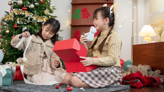 Duas adoráveis jovens asiáticas estão gostando de abrir seu presente de Natal juntas em casa