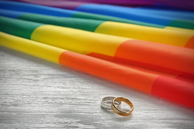 Duas alianças de casamento e bandeira gay de arco-íris em fundo de madeira