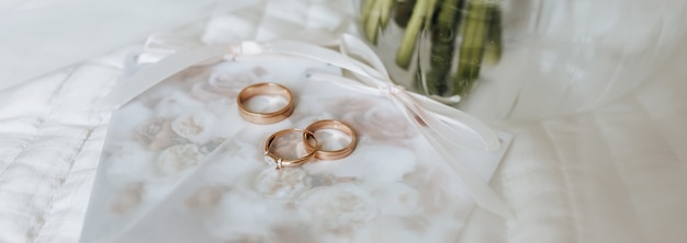 Foto duas alianças de casamento e um anel de noivado repousam em um convite com fundo de flores