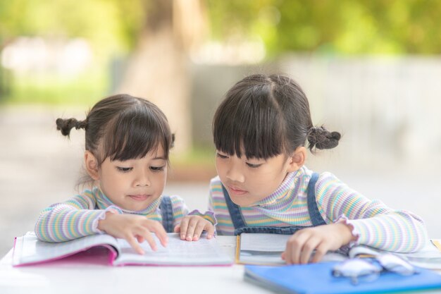 Duas aluna garotas asiáticas lendo o livro sobre a mesa