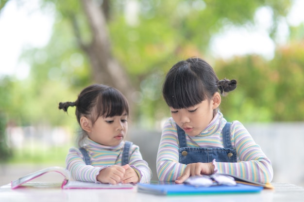 Duas aluna garotas asiáticas lendo o livro sobre a mesa