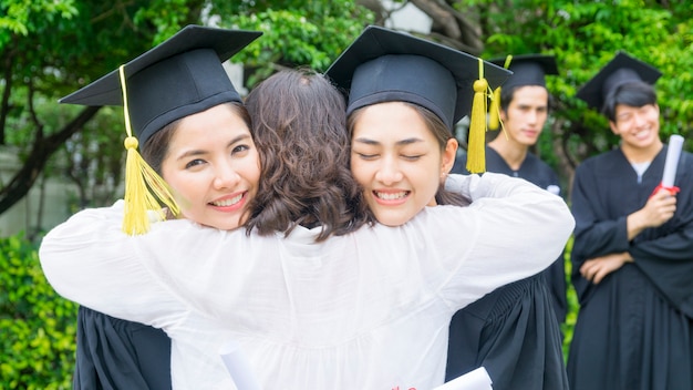 duas alunas asiáticas com os vestidos de formatura abraçam os pais