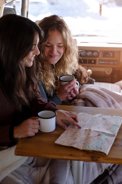 Foto duas amantes tomando café e consultando um mapa em uma van de campista durante a viagem de inverno