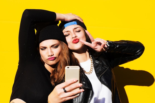 Duas amigas adolescentes com roupa de hipster ao ar livre fazem selfie em um telefone