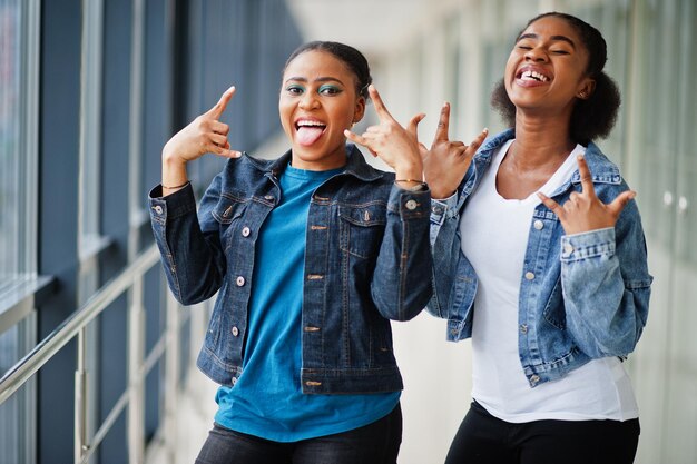 Duas amigas africanas com jaqueta jeans mostram dedos de rocha juntos dentro de casa.