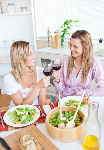 Duas amigas alegres comendo salada na cozinha