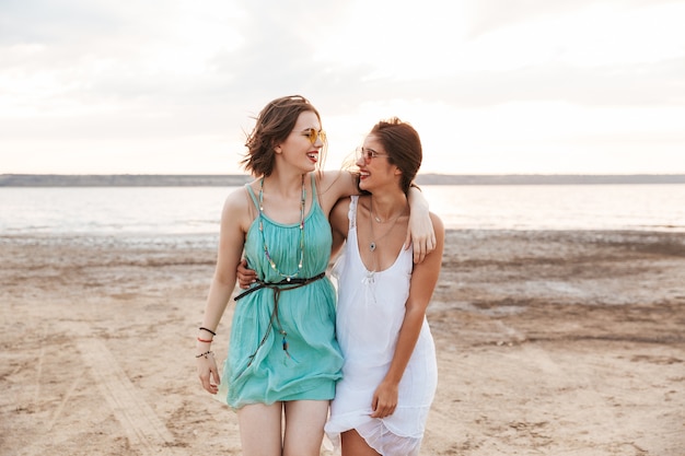 Foto duas amigas alegres passando um bom tempo na praia, rindo