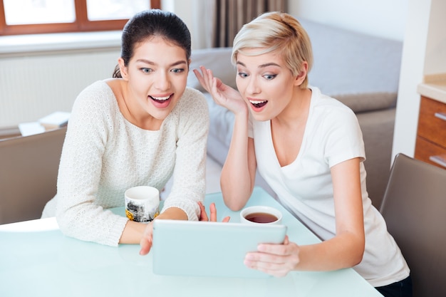 Duas amigas alegres usando um tablet em casa