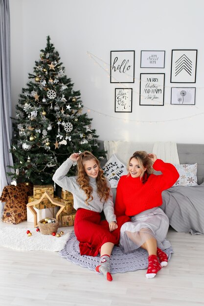 Duas amigas amigas felizes e alegres celebram o Natal perto da árvore de Natal em casa