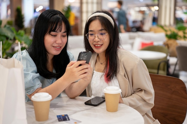 Duas amigas asiáticas estão gostando de conversar enquanto estão sentadas juntas em um café no shopping