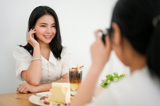 Duas amigas asiáticas felizes aproveitam o fim de semana no café tirando uma foto de amiga com câmera retro