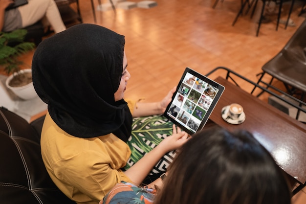 Duas amigas asiáticas usando o tablet e tomando um café na cafeteria