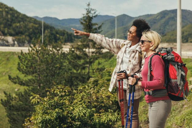 Duas amigas com mochila e bastões de caminhada caminhando nas montanhas em um lindo dia ensolarado de outono.