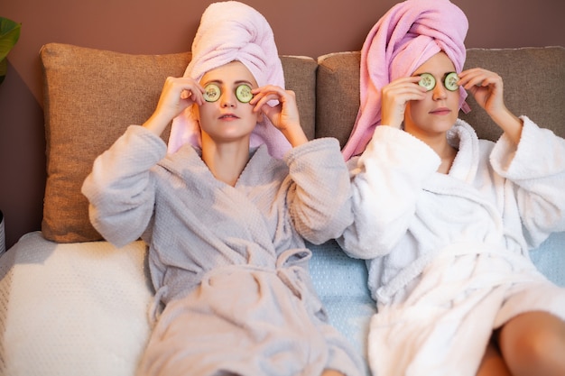 Duas amigas com toalhas na cabeça, fazendo tratamentos de spa em casa na cama