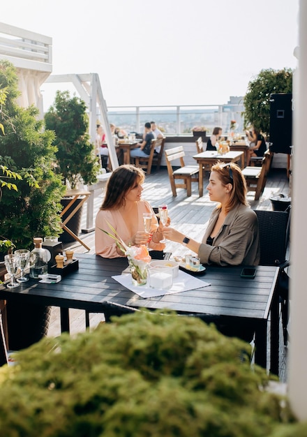 Duas amigas comendo ostras frescas e bebendo vinho prosecco gelado no pôr do sol de verão no restaurante Delícias de frutos do mar