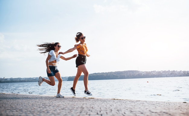 Duas amigas corre e se diverte na praia perto do lago durante o dia ensolarado.