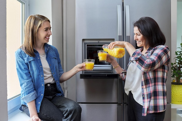 Duas amigas de meia idade bebendo suco de laranja na cozinha