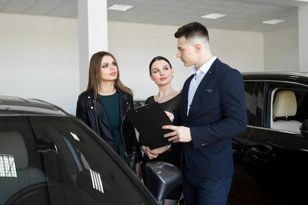 Duas amigas de mulheres com uma concessionária escolhem um carro em uma concessionária