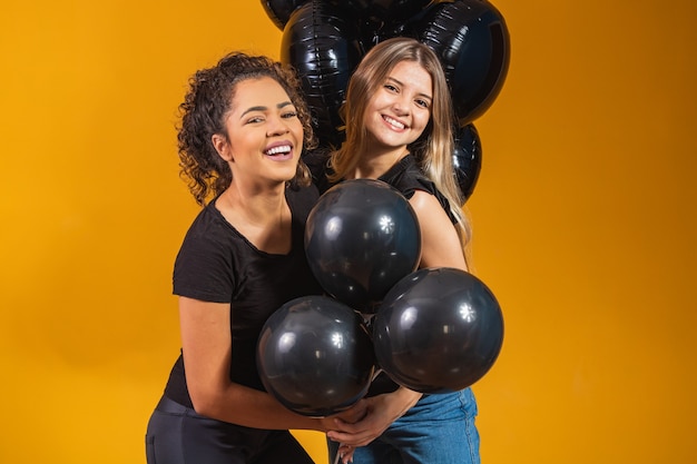 Duas amigas em fundo amarelo com balões pretos na festa de promoção de sexta-feira negra.