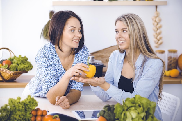 Duas amigas escolhem a receita e os ingredientes para uma refeição deliciosa enquanto estão sentadas à mesa da cozinha Conceito vegetariano