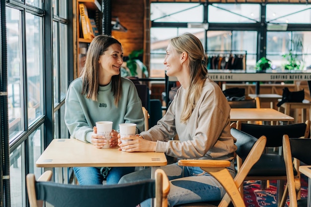 Duas amigas estão conversando e bebendo café enquanto estão sentadas em uma cafeteria