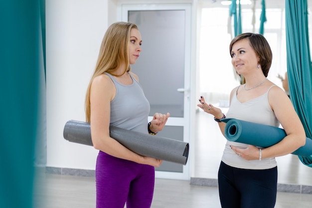 Duas amigas felizes segurando tapete de ioga e prontas para começar a malhar juntos exercícios de ioga ou pilates