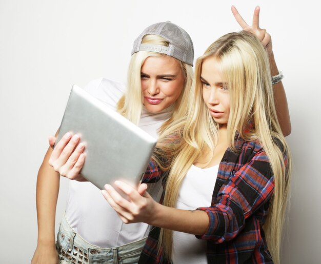 Duas amigas hippie tirando selfie com tablet digital, estúdio filmado sobre fundo cinza