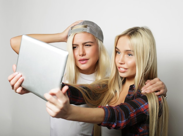 Duas amigas hipster tirando selfie com tablet digital em estúdio filmado em Grey Waccground