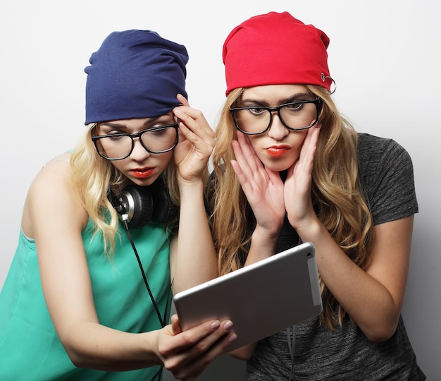 Duas amigas hipster usam estúdio de tablet digital filmado sobre vackground cinza