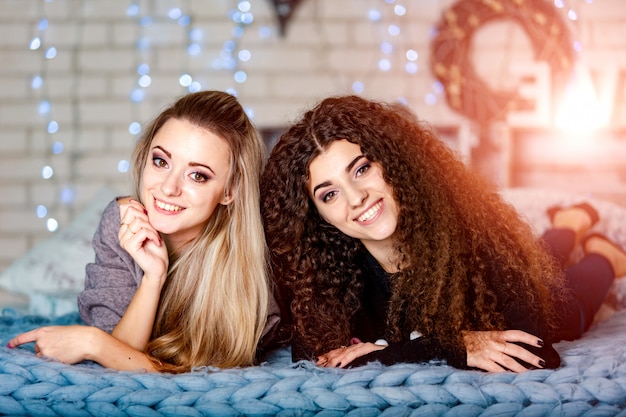 Foto duas amigas lindas felizes em roupas casuais, deitada em um sofá na sala de estar