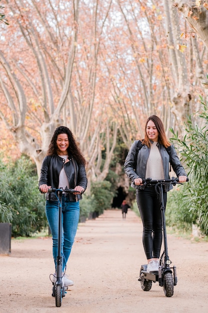 Duas amigas multiétnicas em patinetes elétricas ao ar livre