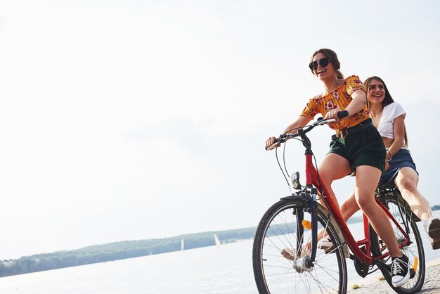 Duas amigas na bicicleta se divertem na praia perto do lago.