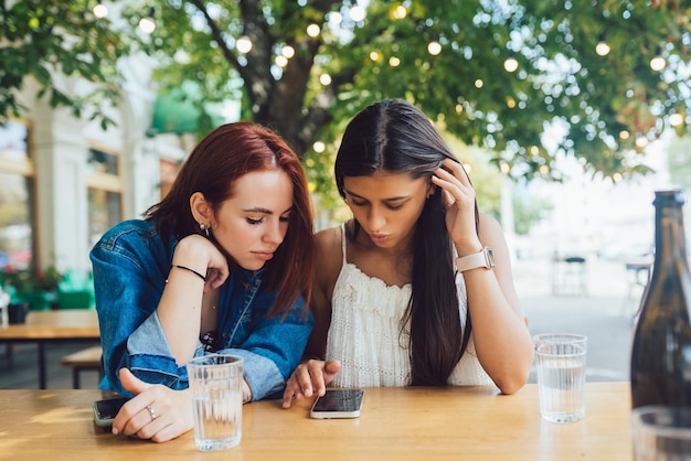 Duas amigas navegando em telefones celulares no café de rua