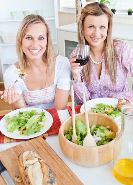 Duas amigas positivas comendo salada na cozinha
