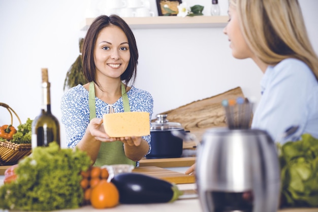 Duas amigas provam novas receitas de fondue delicioso enquanto estão sentadas à mesa da cozinha Conceito de culinária saudável