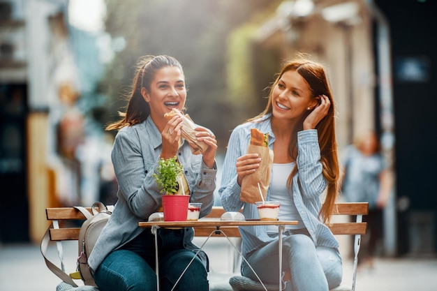 Duas amigas se divertindo ao ar livre comendo sanduíches