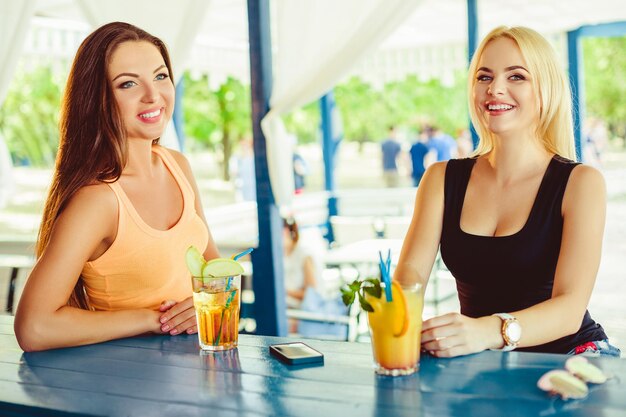 Duas amigas se divertindo ao ar livre em mulheres de verão com copos de coquetel de férias