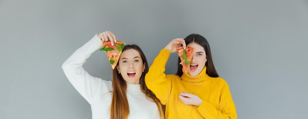 Duas amigas segurando fatias de pizza. Jovens se divertindo jantando.