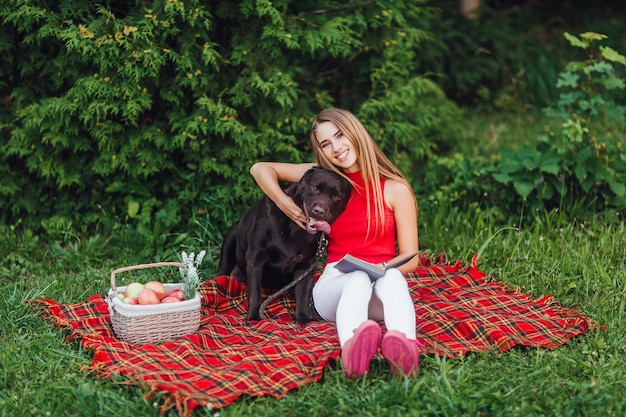 Duas amigas sentadas no cobertor acariciando no jardim, uma mulher loira e seu cachorro