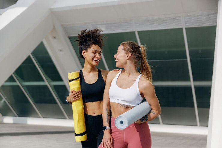 Foto duas amigas sorridente caminhando no fundo da cidade da manhã com tapetes de ioga depois de fazer ginástica da manhã