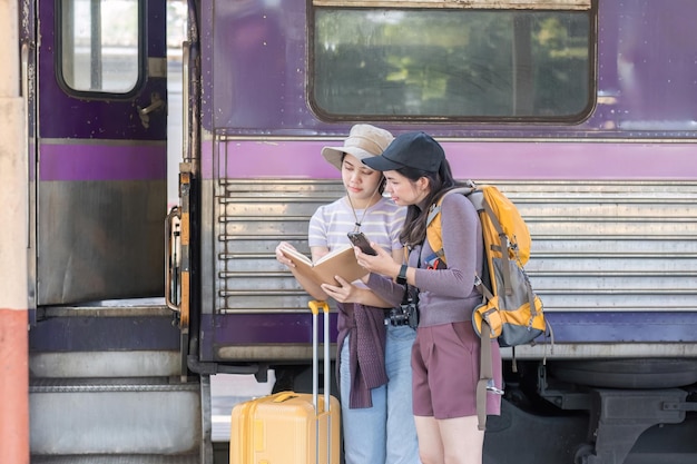 Duas amigas turistas asiáticas estão na estação de comboios à espera do comboio para viajar para o