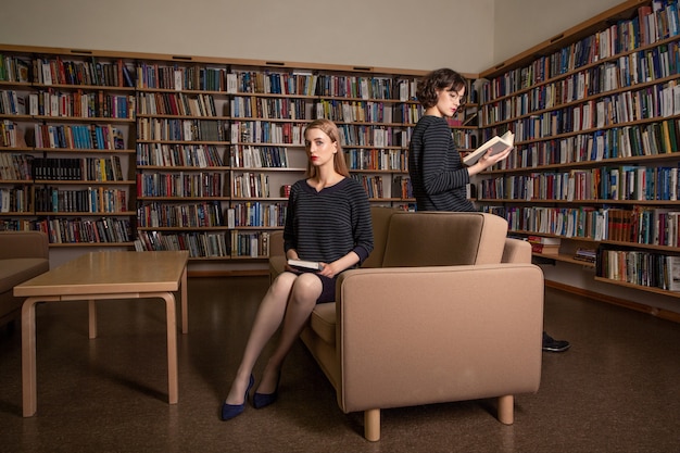 Duas atraentes jovens estudantes do sexo feminino lendo livros na biblioteca.