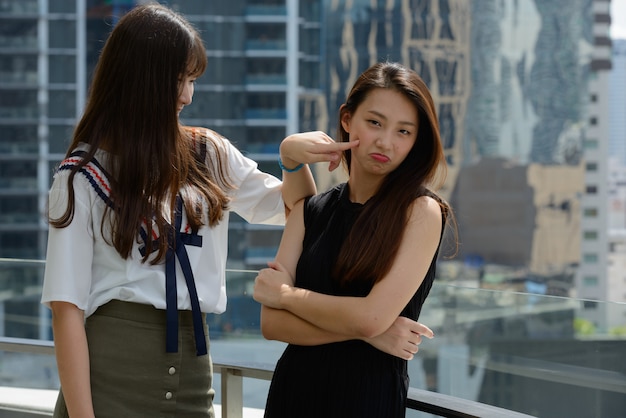 Duas belas jovens adolescentes asiáticas se unindo contra a vista da cidade