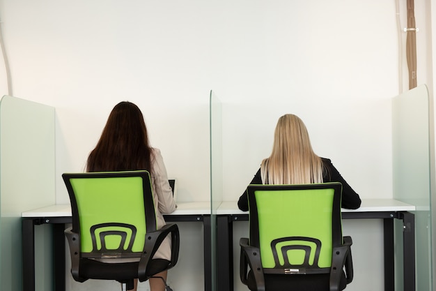 duas belas moças no escritório estão sentadas à mesa de costas