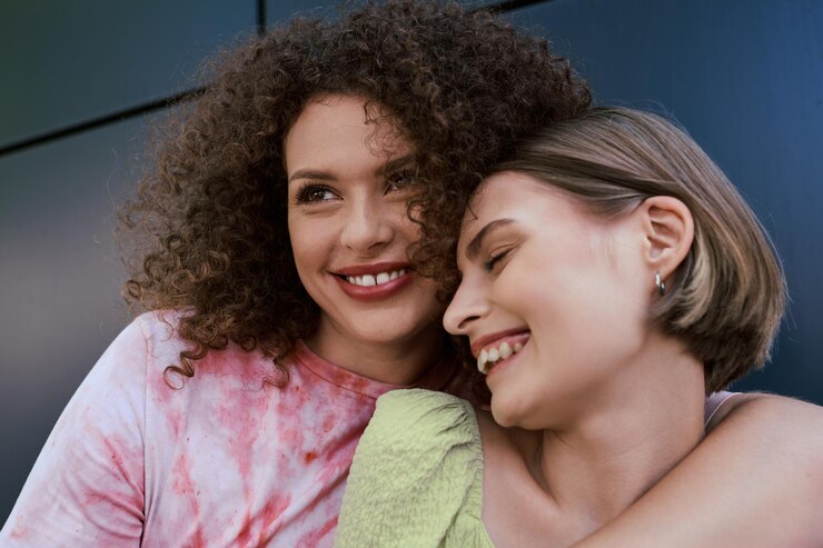 Foto duas belas mulheres jovens compartilham um momento alegre enquanto se abraçam em um cenário urbano ensolarado