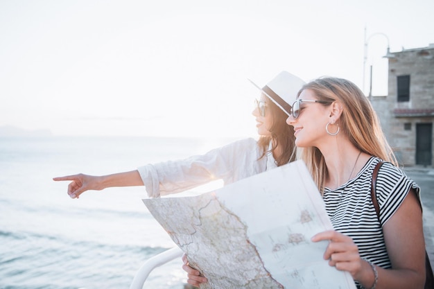 Duas belas mulheres loiras e morenas com mapa turístico de férias. Férias e conceito de turismo