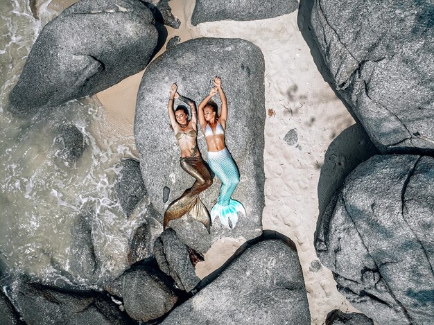 duas belas sereias bronzeadas estão deitadas nas pedras e tomando sol, vista superior