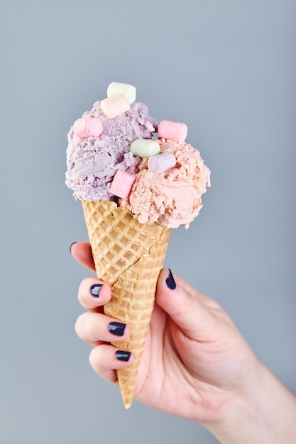 Duas bolas de sorvete no cone de waffle na mão feminina no fundo cinza