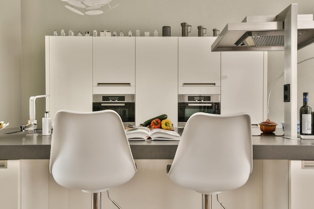 Duas cadeiras brancas em uma cozinha com um livro na bancada e uma porta aberta que leva a outra sala
