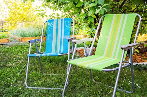 Duas cadeiras dobráveis de jardim ficam à sombra debaixo de uma árvore em um dia quente de verão no jardim fechado